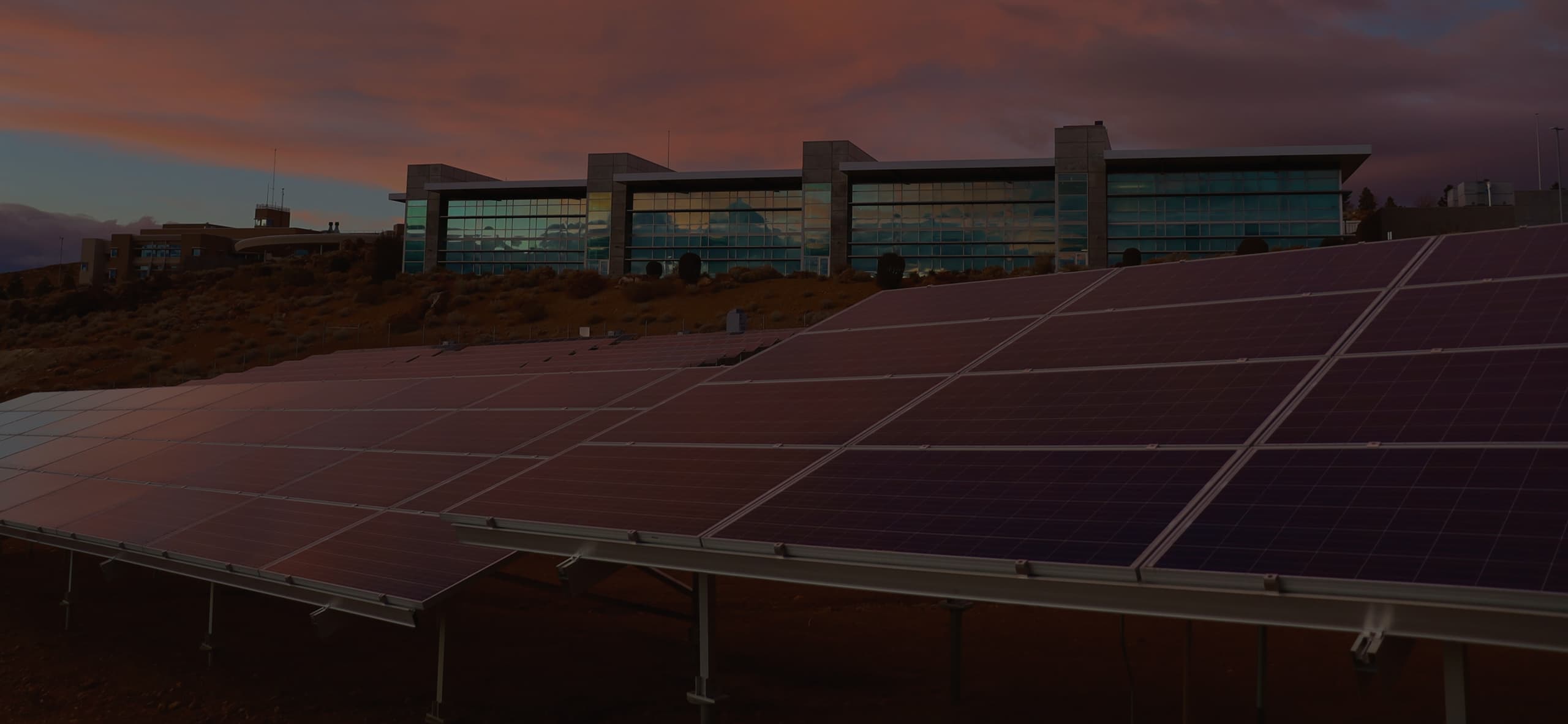 A view of a mirrored corporate office with the sun setting, solar panels in the foreground