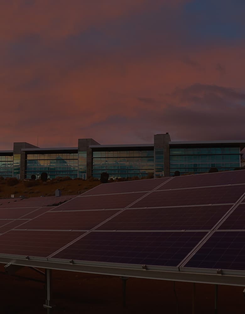 A view of a mirrored corporate office with the sun setting, solar panels in the foreground